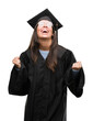 © Krakenimages.com - Young hispanic woman wearing graduated cap and uniform very happy and excited doing winner gesture with arms raised, smiling and screaming for success. Celebration concept.