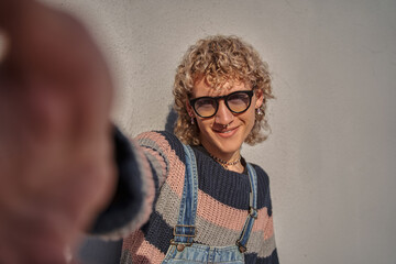 Portrait of jolly young man with pierced nose standing at the street and taking selfie