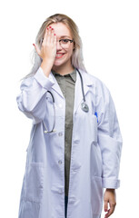 Canvas Print - Young blonde doctor woman over isolated background covering one eye with hand with confident smile on face and surprise emotion.