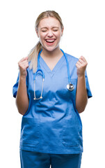 Poster - Young blonde surgeon doctor woman over isolated background excited for success with arms raised celebrating victory smiling. Winner concept.