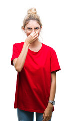 Canvas Print - Young beautiful blonde woman wearing red t-shirt and glasses over isolated background smelling something stinky and disgusting, intolerable smell, holding breath with fingers on nose