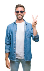 Wall Mural - Young handsome man wearing sunglasses over isolated background smiling with happy face winking at the camera doing victory sign. Number two.