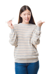 Sticker - Young Chinese woman over isolated background holding aircraft toy pointing and showing with thumb up to the side with happy face smiling