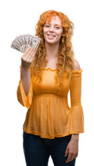 Sticker - Young redhead woman holding dollars with a happy face standing and smiling with a confident smile showing teeth