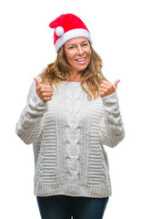 Sticker - Middle age senior hispanic woman wearing christmas hat over isolated background success sign doing positive gesture with hand, thumbs up smiling and happy. Looking at the camera