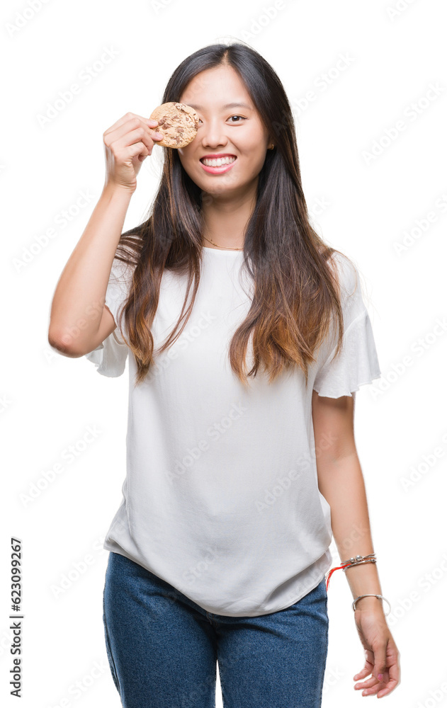 Young asian woman eating chocolate chip cookie over isolated background with a happy face standing and smiling with a confident smile showing teeth