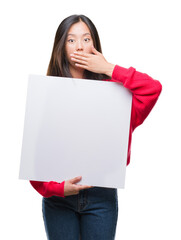 Canvas Print - Young asian woman holding banner over isolated background cover mouth with hand shocked with shame for mistake, expression of fear, scared in silence, secret concept