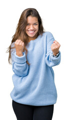 Canvas Print - Young beautiful brunette woman wearing blue winter sweater over isolated background very happy and excited doing winner gesture with arms raised, smiling and screaming for success. Celebration 