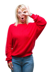 Wall Mural - Young beautiful blonde woman wearing sweater and glasses over isolated background doing ok gesture shocked with surprised face, eye looking through fingers. Unbelieving expression.