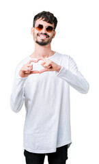 Sticker - Young handsome man wearing sunglasses over isolated background smiling in love showing heart symbol and shape with hands. Romantic concept.