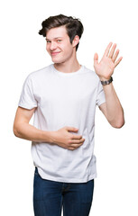 Wall Mural - Young handsome man wearing casual white t-shirt over isolated background Waiving saying hello happy and smiling, friendly welcome gesture