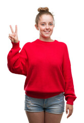 Wall Mural - Young blonde woman wearing bun and red sweater showing and pointing up with fingers number two while smiling confident and happy.