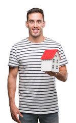 Wall Mural - Handsome real estate agent holding a house with a happy face standing and smiling with a confident smile showing teeth