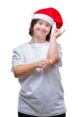 Poster - Young adult woman with down syndrome wearing christmas hat over isolated background with a big smile on face, pointing with hand and finger to the side looking at the camera.