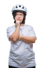 Canvas Print - Young adult cyclist woman with down syndrome wearing safety helmet over isolated background with hand on chin thinking about question, pensive expression. Smiling with thoughtful face. Doubt concept.