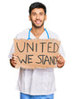 © Krakenimages.com - Young handsome man wearing doctor uniform holding united we stand banner looking positive and happy standing and smiling with a confident smile showing teeth