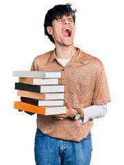 Poster - Handsome hipster young man holding a pile of books angry and mad screaming frustrated and furious, shouting with anger looking up.