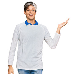 Sticker - Young hispanic man wearing casual clothes smiling cheerful presenting and pointing with palm of hand looking at the camera.