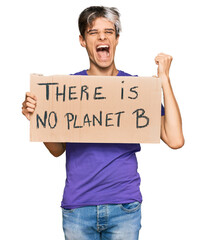 Canvas Print - Young hispanic man holding there is no planet b banner screaming proud, celebrating victory and success very excited with raised arms