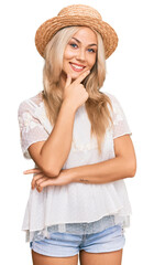 Sticker - Young blonde girl wearing summer hat looking confident at the camera smiling with crossed arms and hand raised on chin. thinking positive.