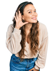 Sticker - Young hispanic girl wearing casual clothes smiling with hand over ear listening and hearing to rumor or gossip. deafness concept.