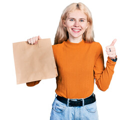 Poster - Young caucasian woman holding take away paper bag smiling happy and positive, thumb up doing excellent and approval sign