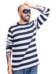 Poster - Young handsome man wearing burglar mask smiling confident touching hair with hand up gesture, posing attractive and fashionable