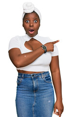 Wall Mural - Young african woman with turban wearing hair turban over isolated background surprised pointing with finger to the side, open mouth amazed expression.