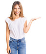 © Krakenimages.com - Beautiful caucasian woman with blonde hair wearing casual white tshirt smiling cheerful presenting and pointing with palm of hand looking at the camera.