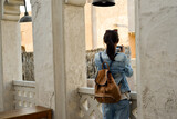 Fototapeta Uliczki - A young woman traveler with a backpack on her back walks and photographs the old narrow streets of Dubai Deira and Creek. Travel and sightseeing concept.