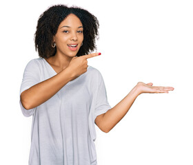 Wall Mural - Young african american girl wearing casual clothes amazed and smiling to the camera while presenting with hand and pointing with finger.