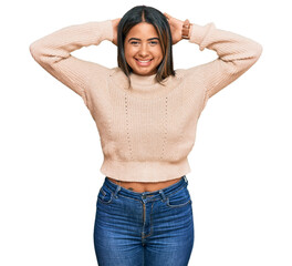 Sticker - Young latin girl wearing wool winter sweater relaxing and stretching, arms and hands behind head and neck smiling happy