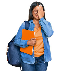 Canvas Print - Young latin girl wearing student backpack and holding books covering one eye with hand, confident smile on face and surprise emotion.