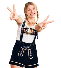 Wall Mural - Young beautiful blonde woman wearing oktoberfest dress smiling with tongue out showing fingers of both hands doing victory sign. number two.