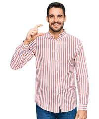 Wall Mural - Young hispanic man wearing business shirt smiling and confident gesturing with hand doing small size sign with fingers looking and the camera. measure concept.