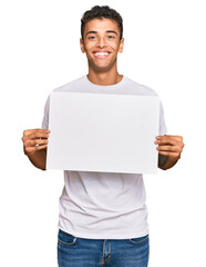 Poster - Young handsome african american man holding blank empty banner looking positive and happy standing and smiling with a confident smile showing teeth