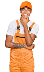 Poster - Young handsome african american man wearing handyman uniform looking confident at the camera smiling with crossed arms and hand raised on chin. thinking positive.