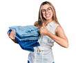 © Krakenimages.com - Hispanic young woman holding stack of folded jeans smiling happy and positive, thumb up doing excellent and approval sign