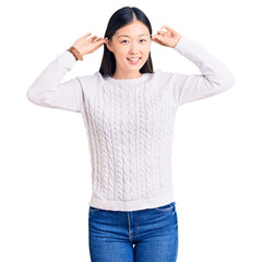 Wall Mural - Young beautiful chinese woman wearing casual sweater smiling pulling ears with fingers, funny gesture. audition problem