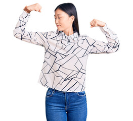 Poster - Young beautiful chinese woman wearing casual shirt showing arms muscles smiling proud. fitness concept.