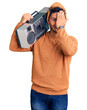 © Krakenimages.com - Handsome latin american young man holding boombox, listening to music covering one eye with hand, confident smile on face and surprise emotion.