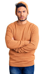 Handsome latin american young man wearing winter sweater and wool hat skeptic and nervous, disapproving expression on face with crossed arms. negative person.