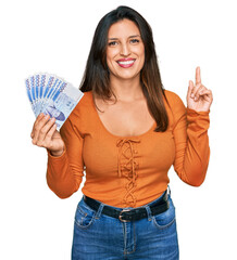 Sticker - Beautiful hispanic woman holding 1000 south korean won banknotes surprised with an idea or question pointing finger with happy face, number one