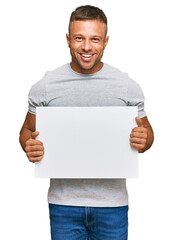 Wall Mural - Handsome muscle man holding blank empty banner looking positive and happy standing and smiling with a confident smile showing teeth