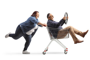 Wall Mural - Full length profile shot of a woman pushing a mature man with a steering wheel inside a shopping cart