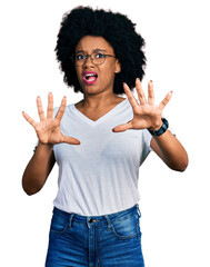 Poster - Young african american woman wearing casual white t shirt afraid and terrified with fear expression stop gesture with hands, shouting in shock. panic concept.