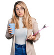 Young blonde woman wearing business style, drinking coffee and holding clipboard clueless and confused expression. doubt concept.
