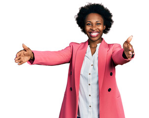 Wall Mural - African american woman with afro hair wearing business jacket looking at the camera smiling with open arms for hug. cheerful expression embracing happiness.