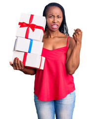 Canvas Print - Young african american woman holding gift annoyed and frustrated shouting with anger, yelling crazy with anger and hand raised