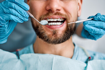 cropped portrait of handsome man with braces sitting in dental chair. doctor in gloves holding exami